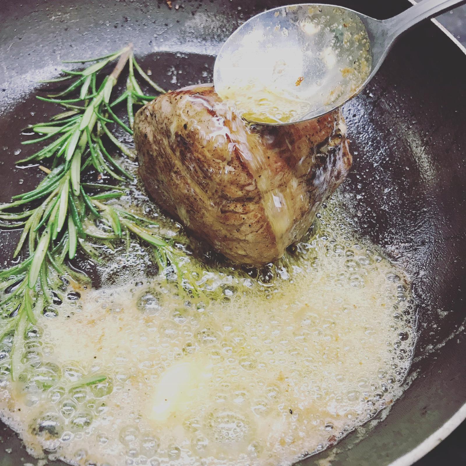 Beef fillet being basted with rosemary butter in a cast iron pan
